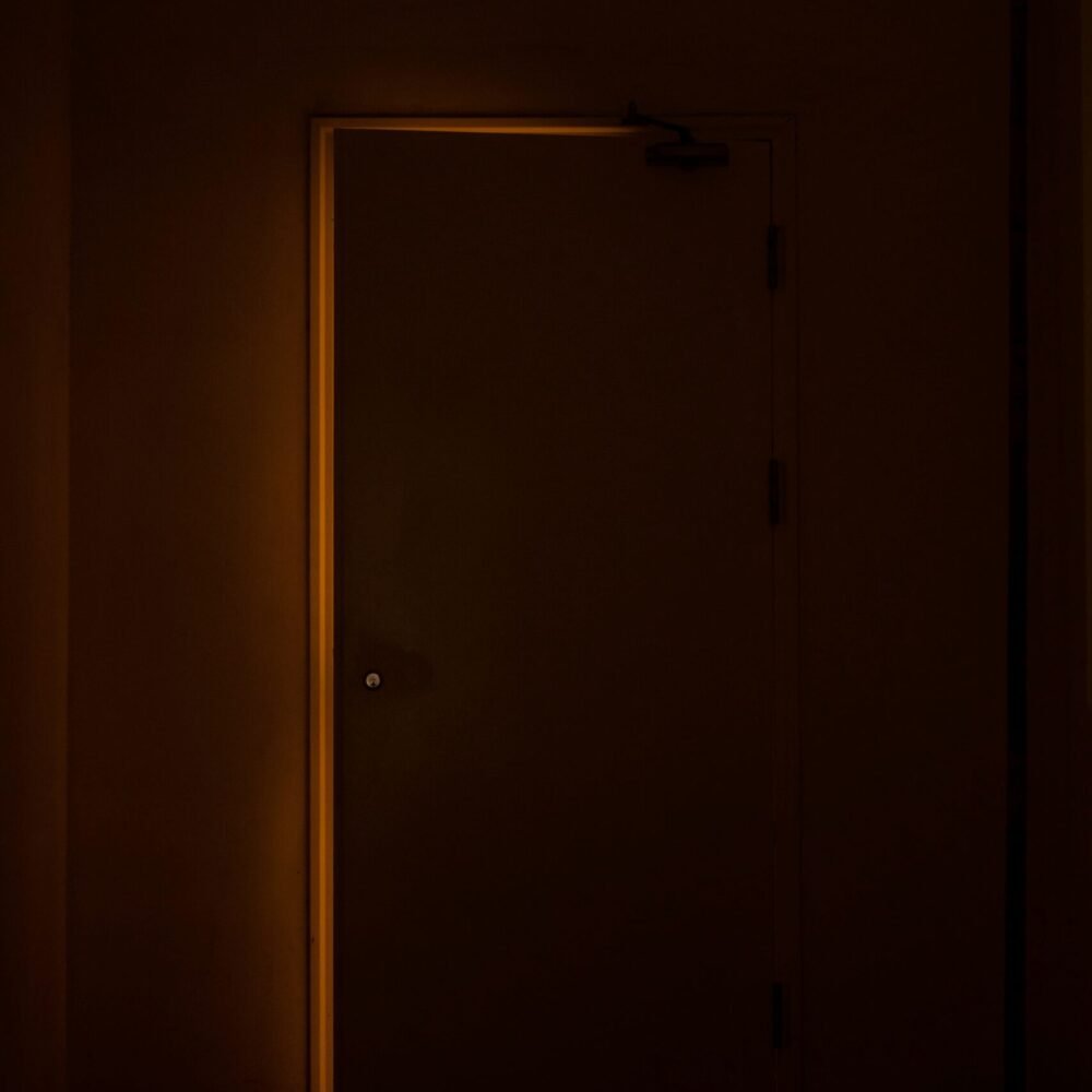Dark closed door with warm golden light shining around its edges